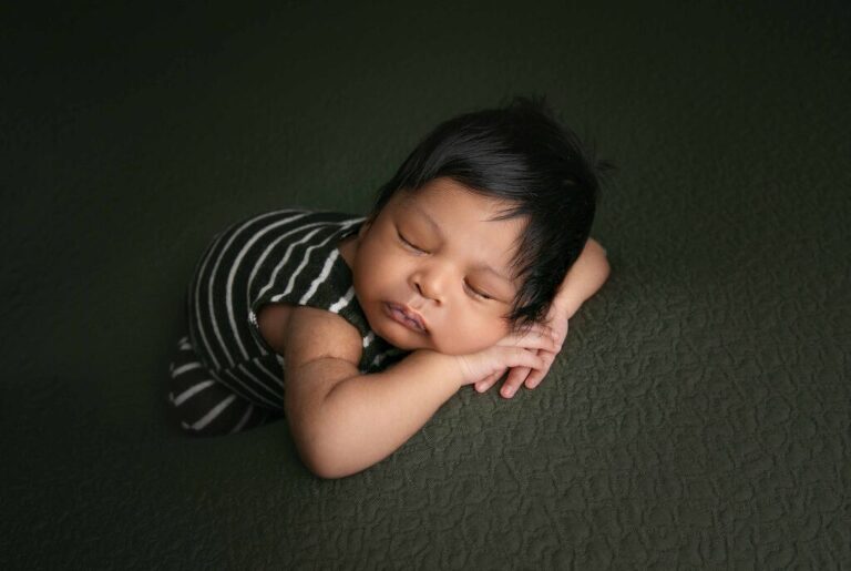 Newborn baby boy with lots of black hair on a dark green backdrop 