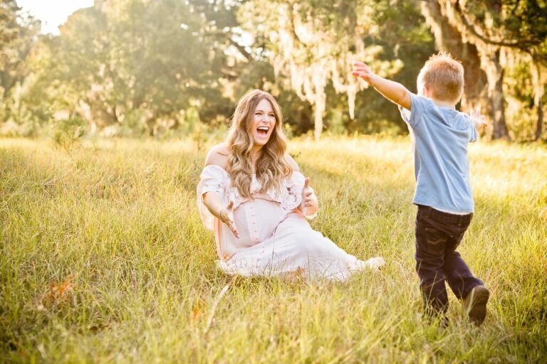 pregnant mother in a sun soaked field reaching out for her little boy running towards her