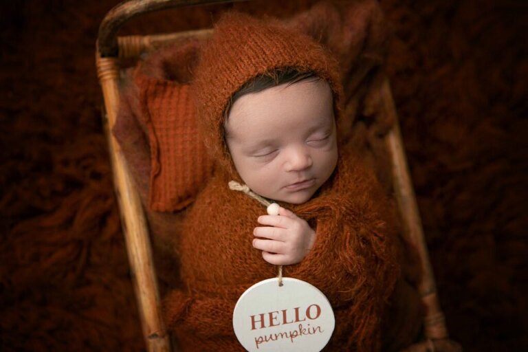 newborn baby in orange wrap holding a Hello Pumpkin sign 