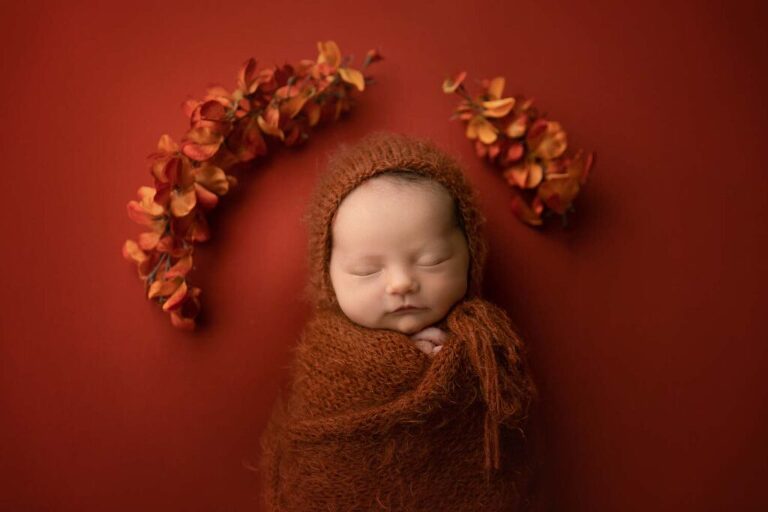 baby wrapped in a rust colored knit wrap with fall colored flowers