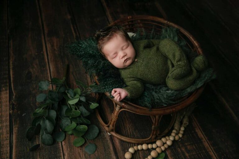 newborn baby wearing a dark green outfit with greenery 